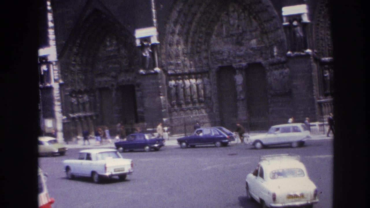 1967 Paris intersection with white and blue vintage cars moving past the ornate stone cathedral facade.
