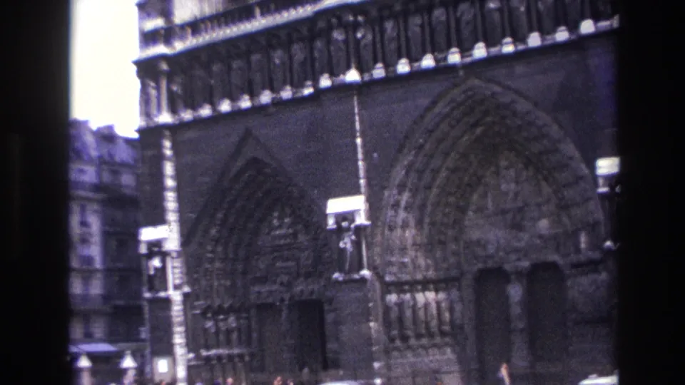1967 Paris home-movie frame showing Notre-Dame Cathedral portals, carved arches and a dark vertical frame edge.