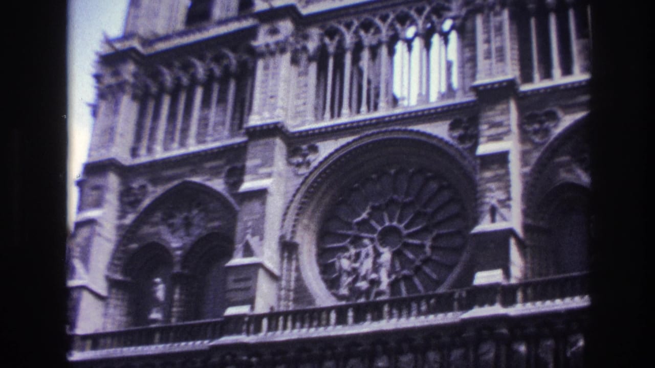1967 Paris home-movie frame showing Notre-Dame Cathedral façade details, including the rose window, arches and carved stone figures.