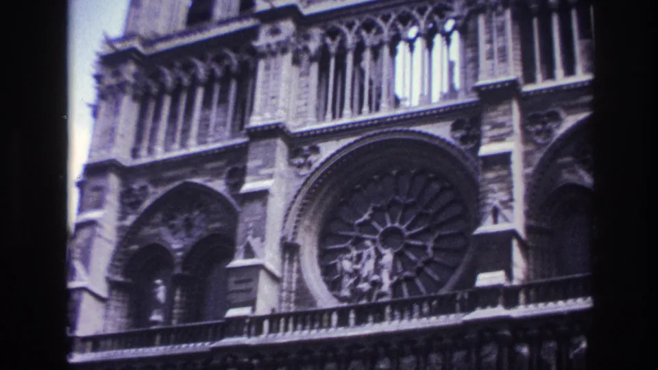 1967 Paris home-movie frame showing Notre-Dame Cathedral façade details, including the rose window, arches and carved stone figures.