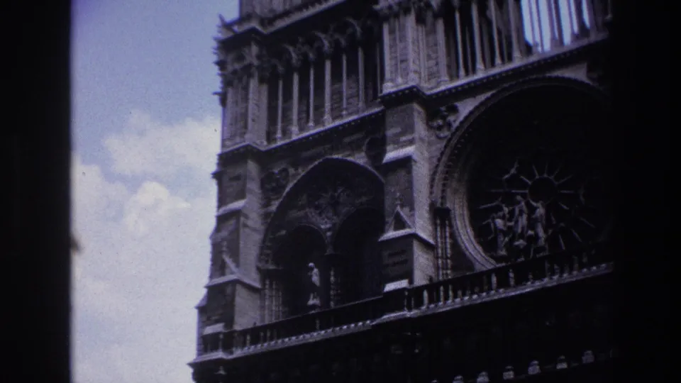 Handheld 1967 Paris view of Notre-Dame Cathedral, with pale sky beside darkened stone arches and part of the rose window.