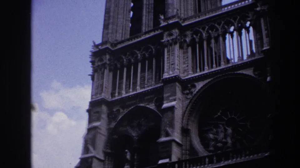 1967 Paris home-movie frame showing Notre-Dame tower masonry, upper tracery, arched stonework and part of the rose window.