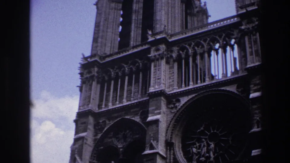 1967 Paris home-movie frame showing a low-angle Notre-Dame Cathedral facade with stone tracery, towers, and dark film gate edges.