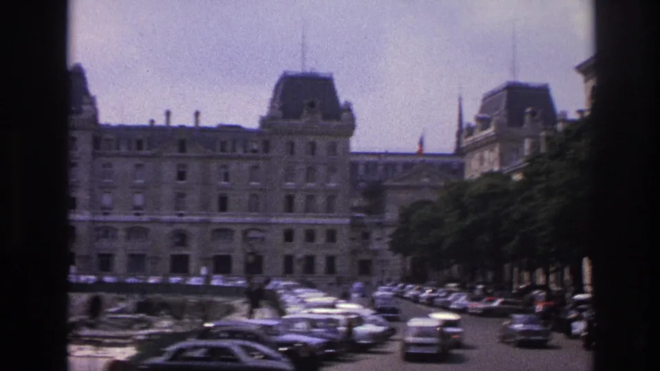 1967 Paris street view of a large historic stone building, rows of cars, and dark vertical window framing.