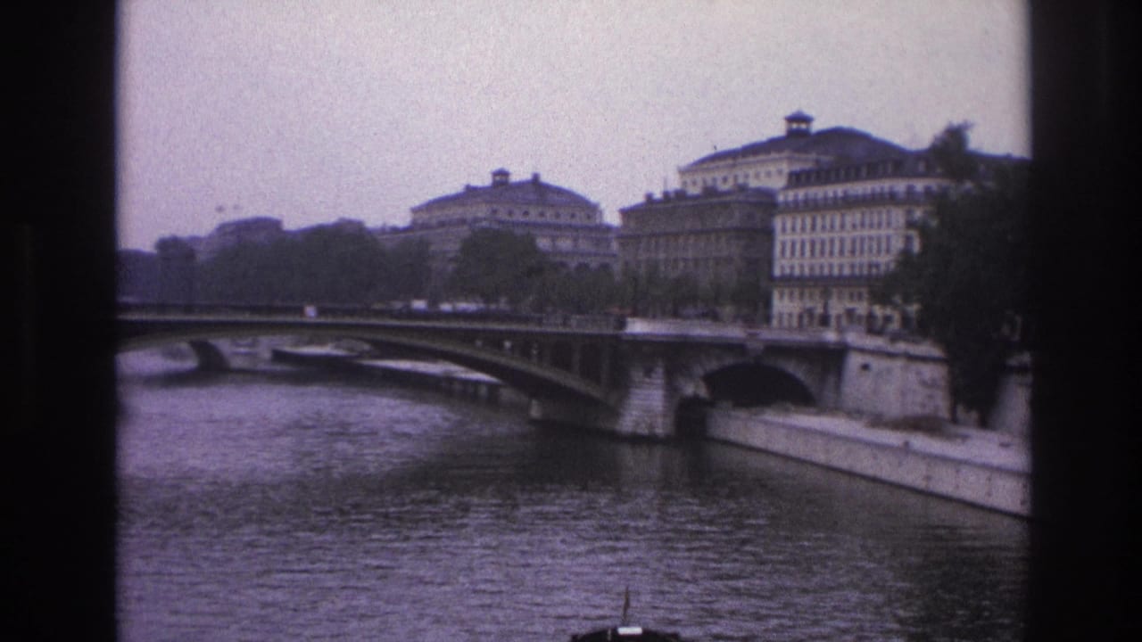 1967 Paris home-movie frame showing the Seine, an arched bridge, riverfront buildings, trees, and vertical dark borders.