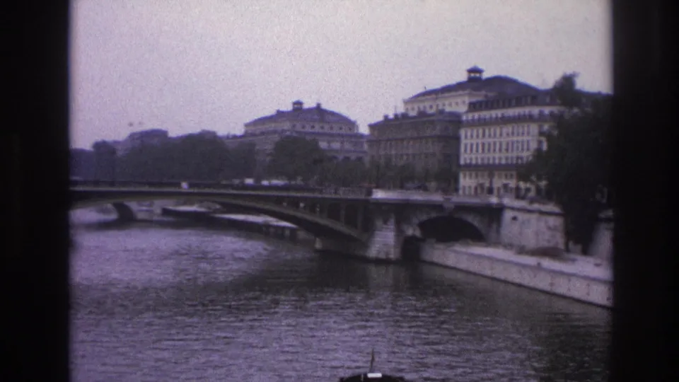 1967 Paris home-movie frame showing the Seine, an arched bridge, riverfront buildings, trees, and vertical dark borders.