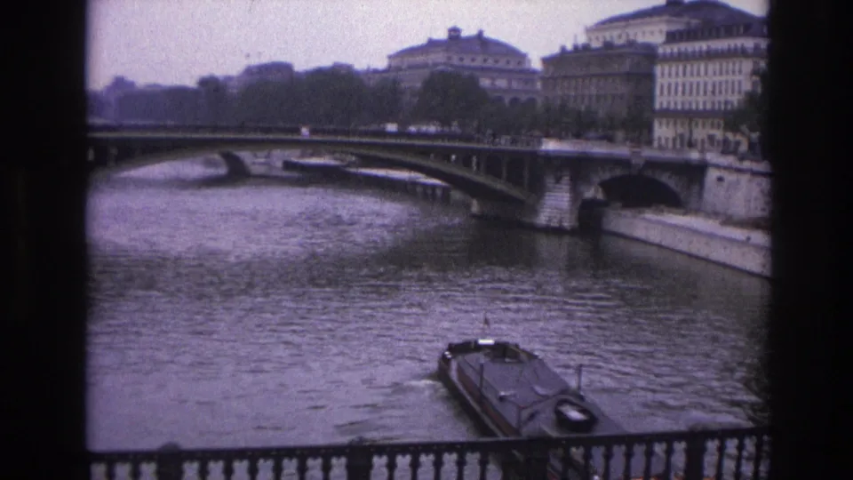 1967 Paris home-movie frame with a narrowboat moving on the Seine below a bridge and riverside architecture.