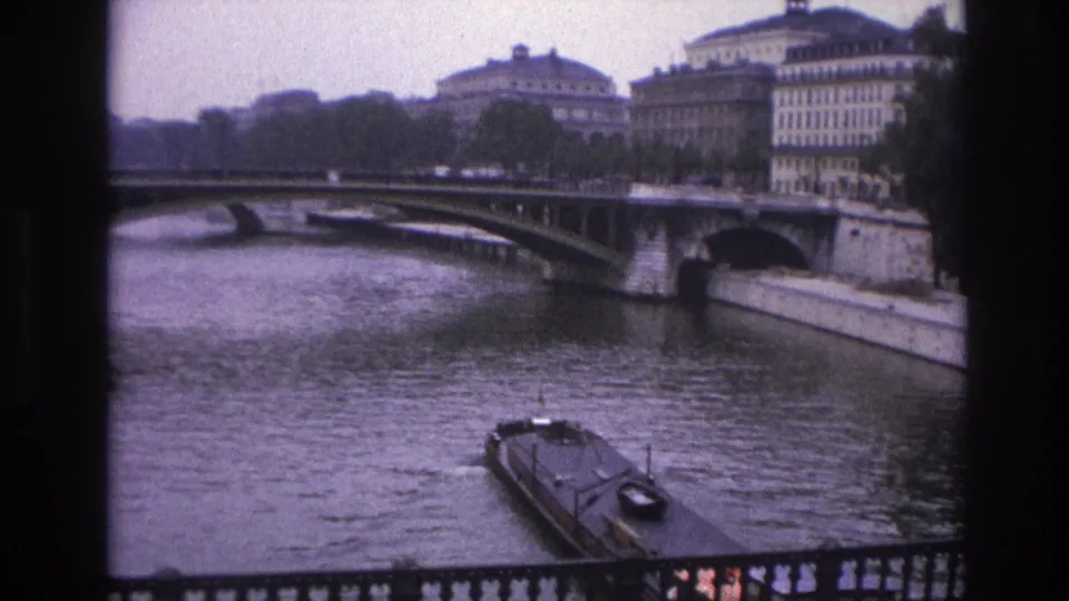 1967 Paris frame showing the Seine, a narrowboat near the foreground railing, a bridge, and soft-focus riverfront buildings.