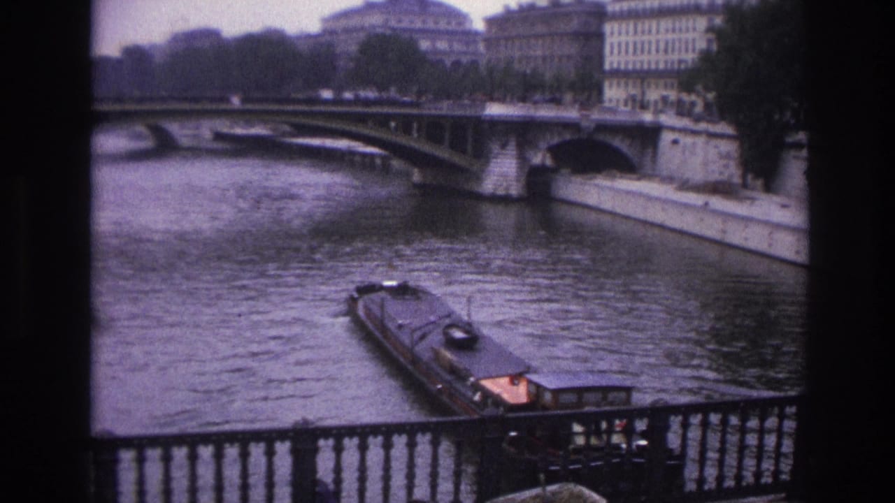 Barge approaching the foreground with bridge, riverbank, buildings, and railing visible.