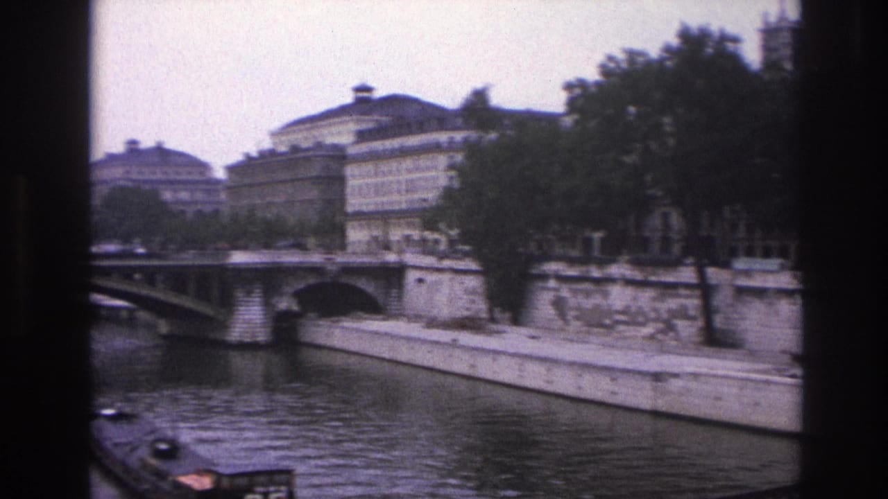 1967 Paris 8mm frame from the Seine showing a bridge, riverside buildings, trees, stone quay walls, and part of a barge.