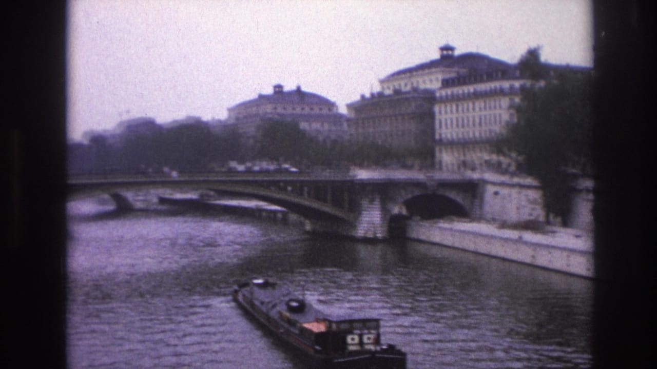 Barge on the Seine approaching a bridge with large buildings and trees along both banks.
