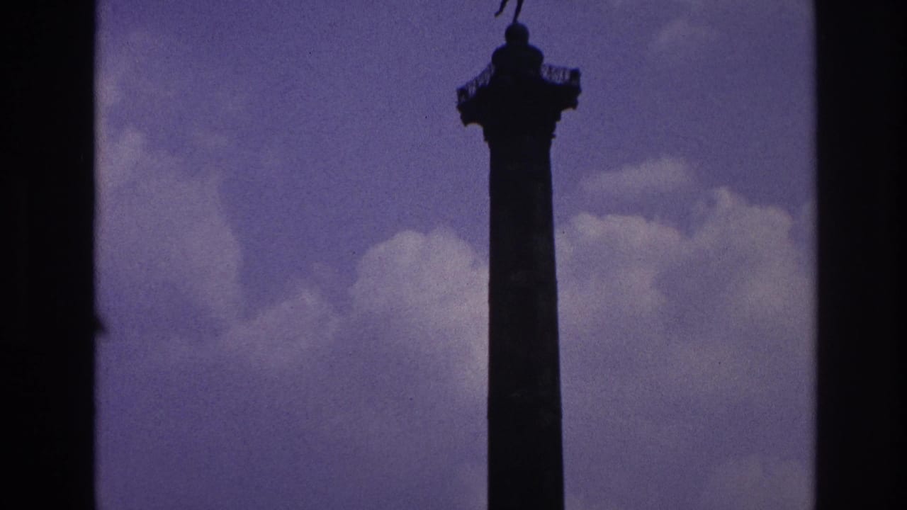 Tall Paris monument column with a statue at the top, filmed against a purple-blue sky in aged 8mm color.
