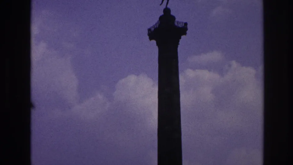 Tall Paris monument column with a statue at the top, filmed against a purple-blue sky in aged 8mm color.