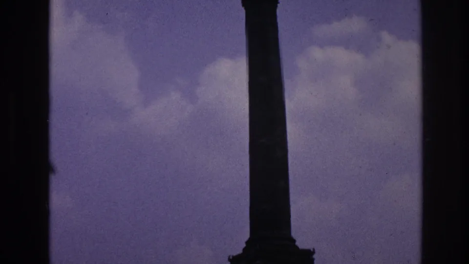 Vertical view of a Paris monument column and base, framed tightly with cloudy sky and dark film borders.
