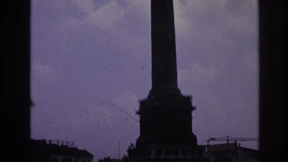 A tall Paris monument column and base are shown with surrounding rooftops under a purple-blue sky.