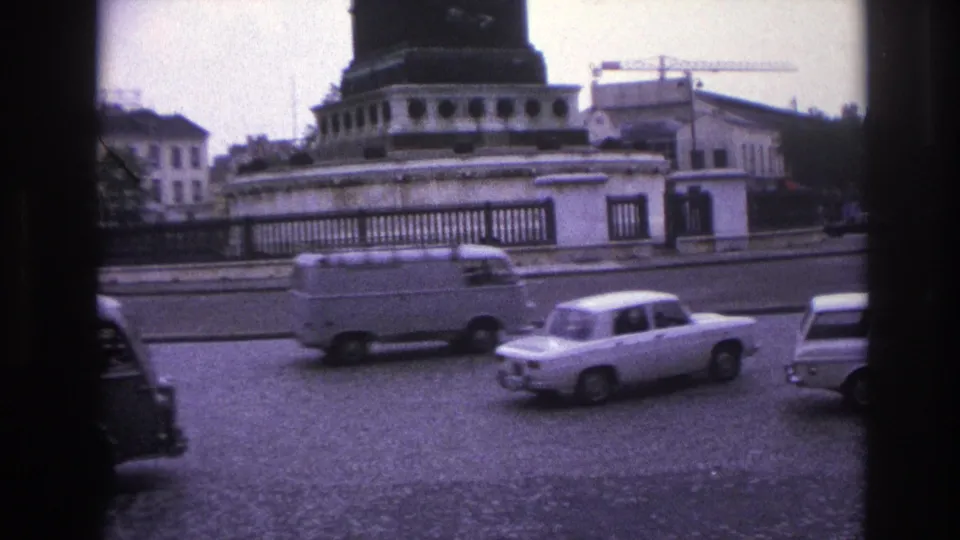 1967 Paris frame showing mid-century cars and a van moving along a broad roadway below a prominent monument base.