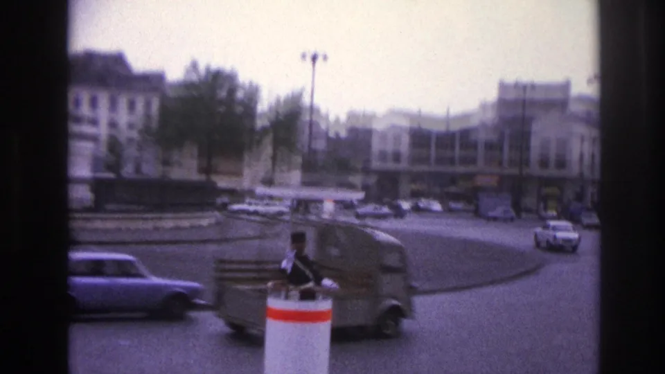 1967 Paris frame showing a uniformed traffic officer on a red-and-white control post with vans and cars moving through the roundabout.