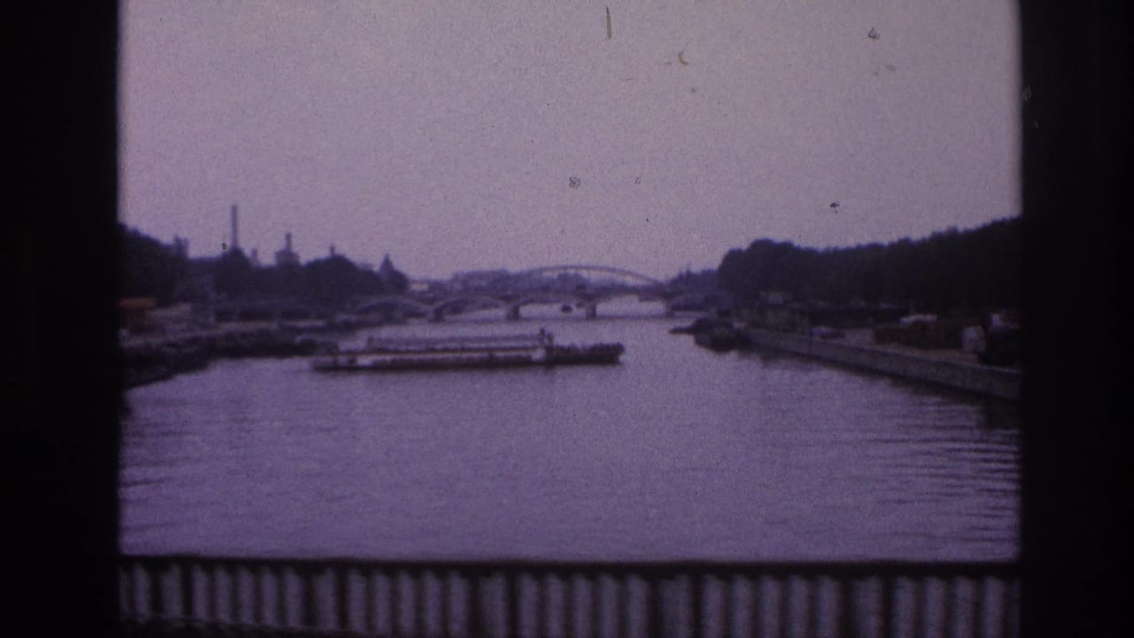 A 1967 Paris river view shows a freight barge below a distant arched bridge, with industrial structures and dark tree lines along the banks.