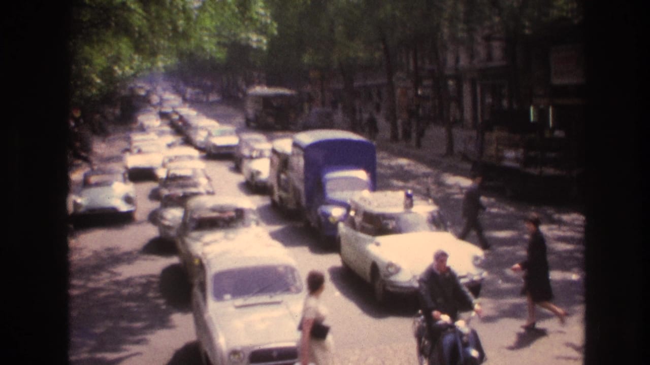 1967 Paris street scene viewed from an upper level, showing mid-century cars, pedestrians, and a scooter rider on a tree-lined boulevard.