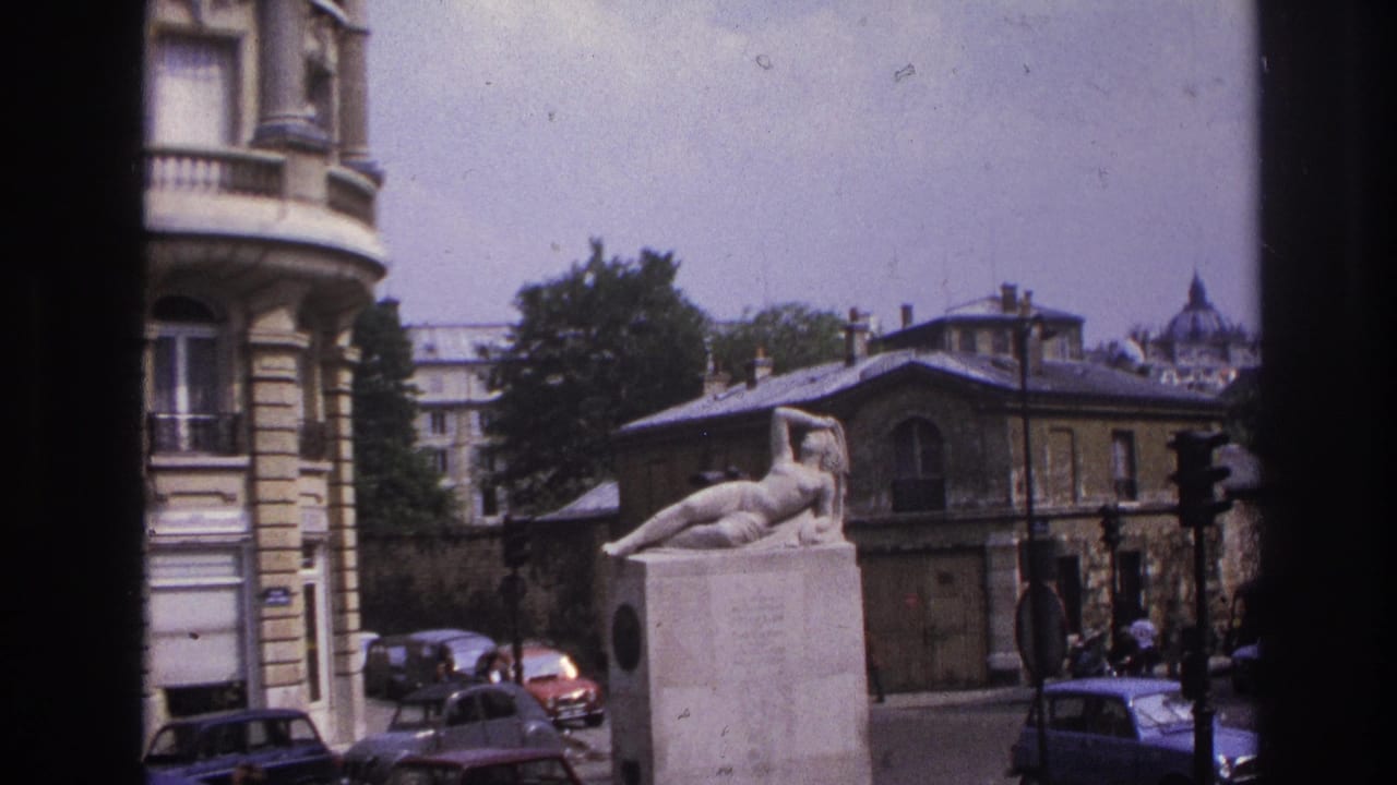 1967 Paris street view with a reclining nude statue on a pedestal, parked cars, pedestrians, and stone apartment facades.