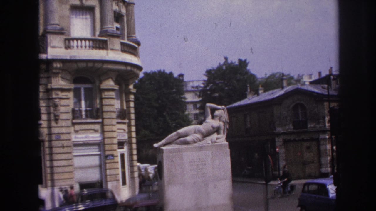 Reclining nude statue and nearby buildings seen through a dark window frame.
