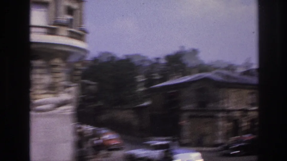 Motion-blurred 1967 Paris street frame with the reclining statue at left, cars below, and buildings shifting during a handheld pan.