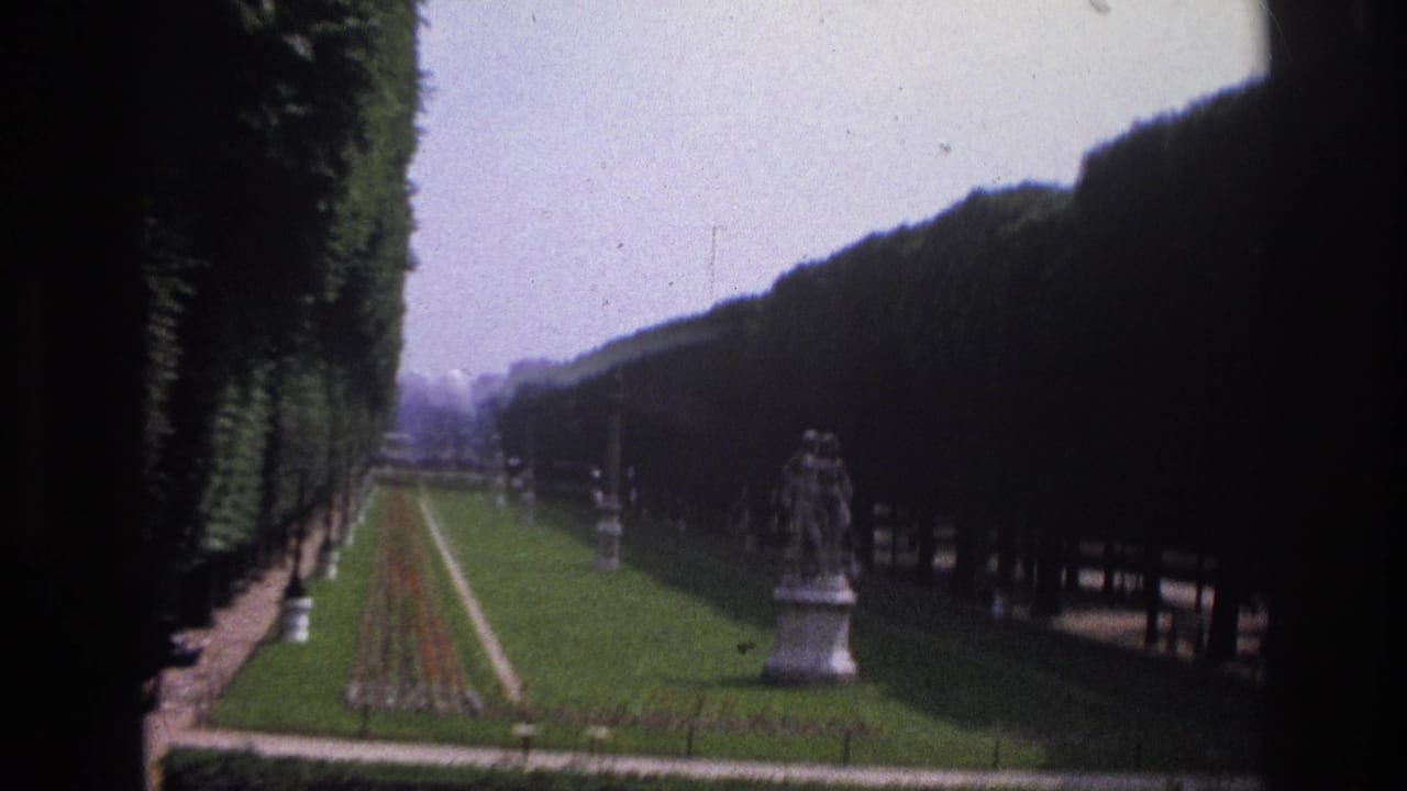 1967 Paris home-movie view of a formal garden with clipped hedges, a central flowerbed, and a classical statue.
