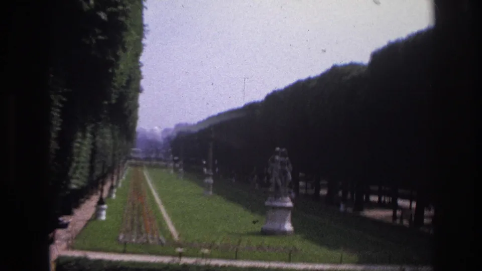 1967 Paris home-movie view of a formal garden with clipped hedges, a central flowerbed, and a classical statue.