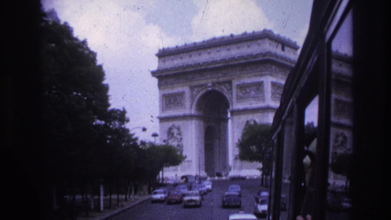 1967 Paris street view toward the Arc de Triomphe, filmed past a vehicle window with cars ahead.