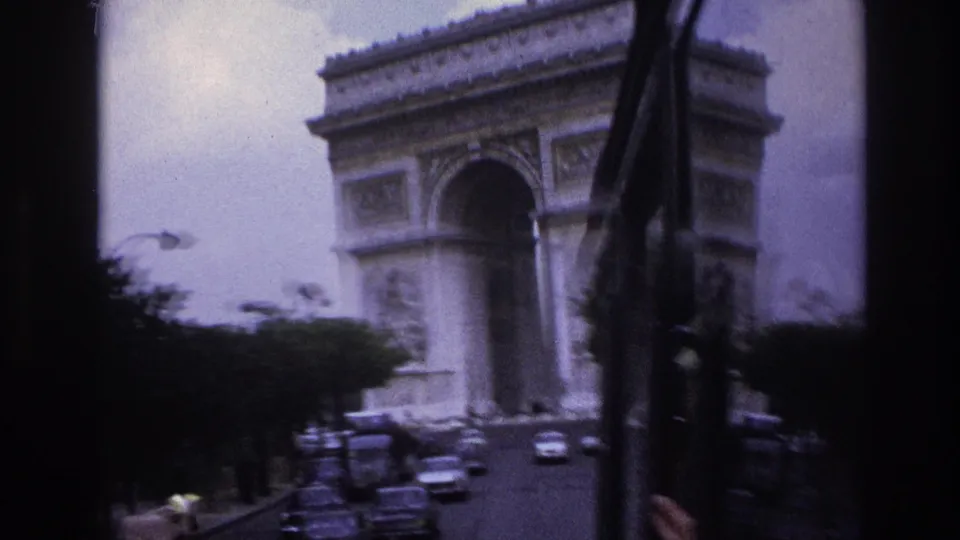 Blurred 1967 Paris travel footage shows the Arc de Triomphe through a moving vehicle window, with cars gathered on the street below.