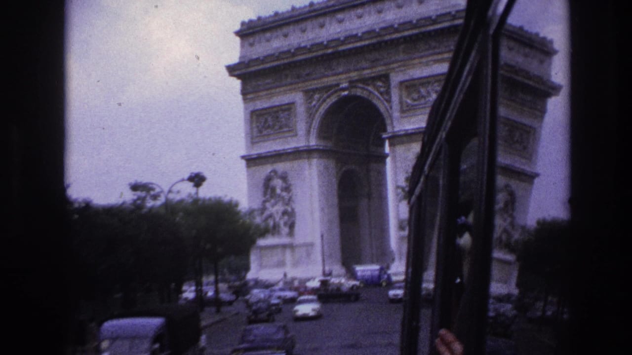 Arc de Triomphe seen from a moving vehicle with traffic and trees in the foreground.