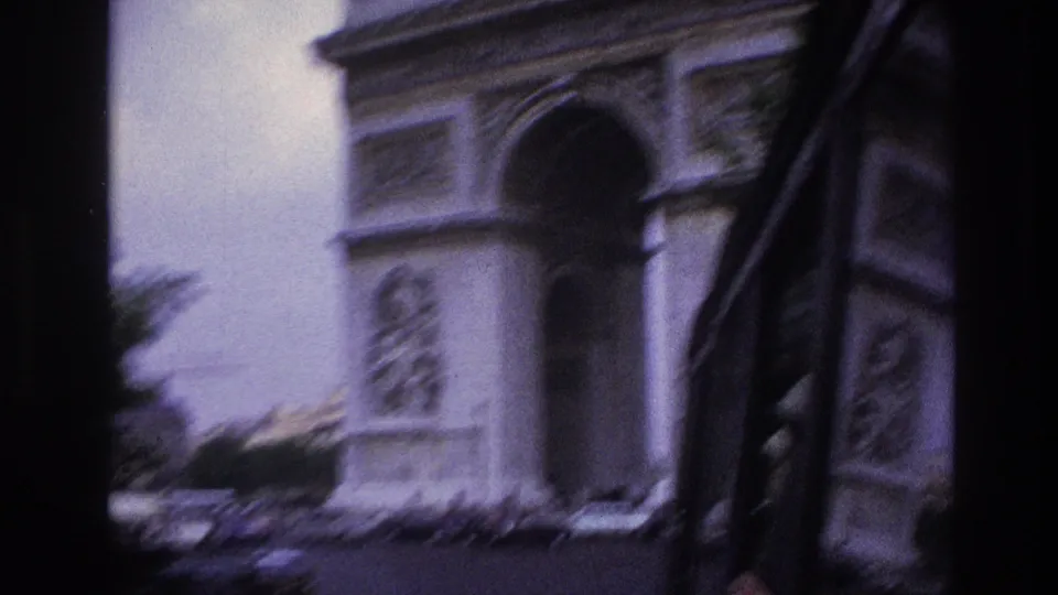 The Arc de Triomphe passes through frame in 1967 Paris footage, partially obscured by vehicle-window framing and motion blur.