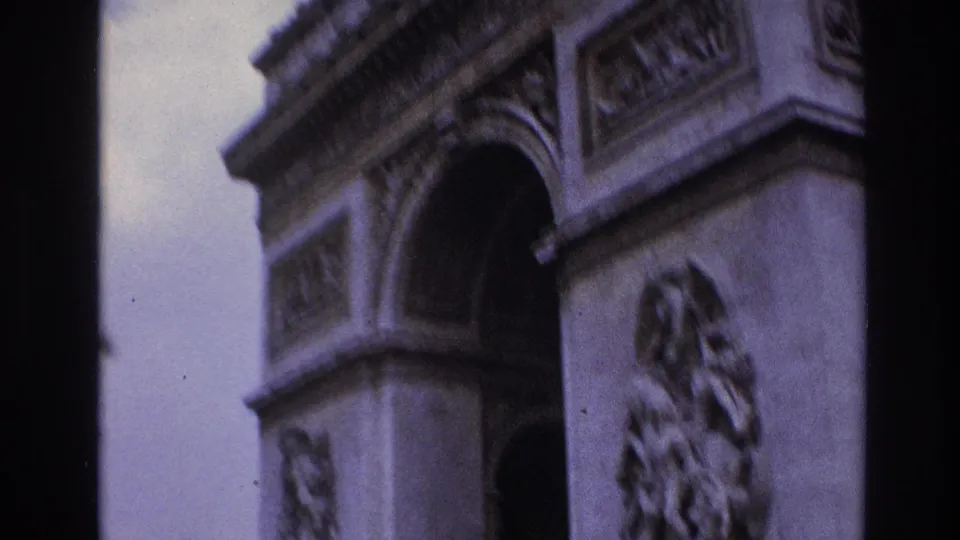 A tilted 1967 Paris frame shows the Arc de Triomphe at close range, with sculptural reliefs, stonework, and dark vehicle framing at right.