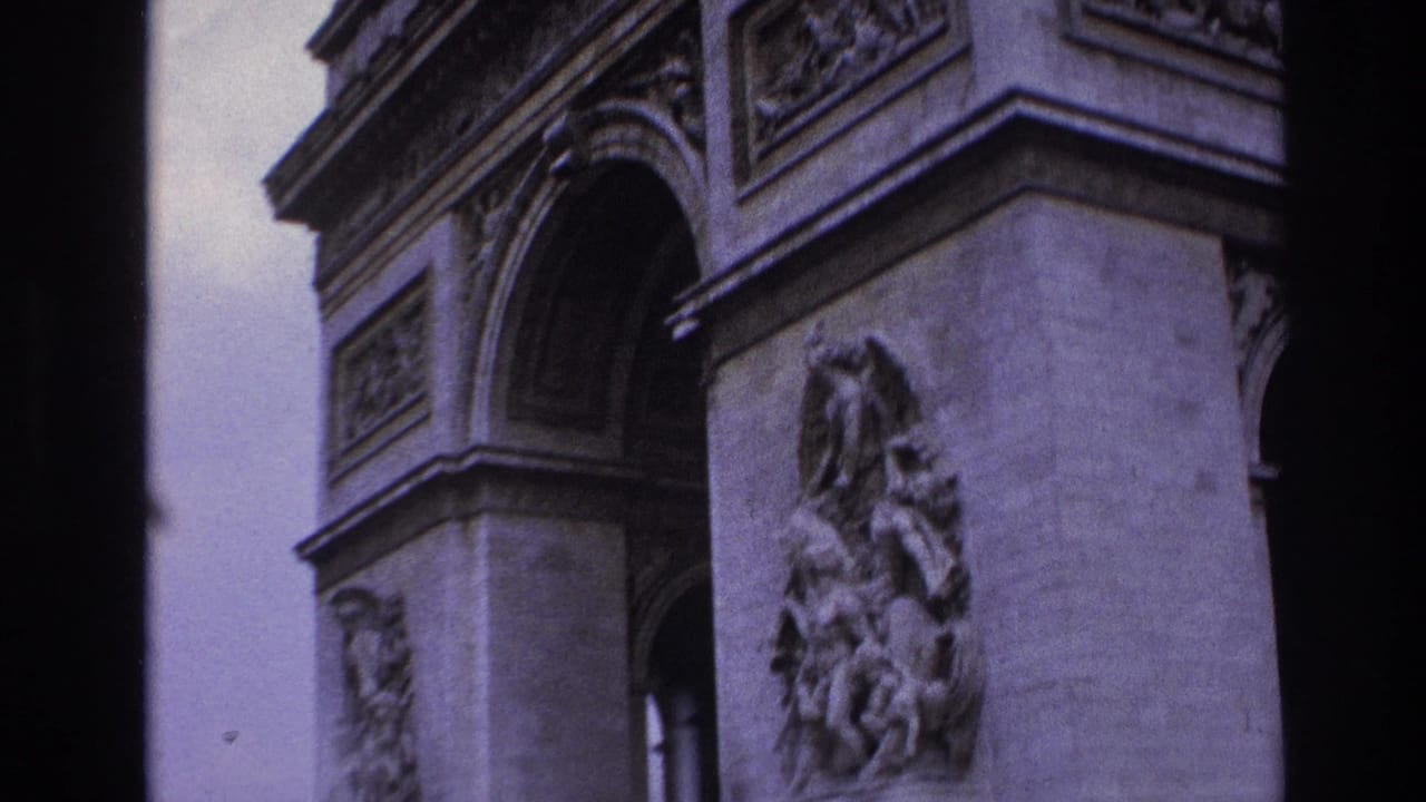 1967 Paris home-movie frame showing the Arc de Triomphe with a large sculpted relief, arch opening, carved frieze, and purple-tinted film color.
