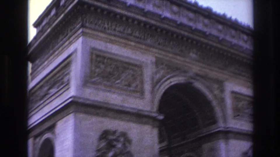 Purple-tinted 8mm Paris frame showing the upper Arc de Triomphe facade with a large arch opening, carved frieze, and relief sculpture below.