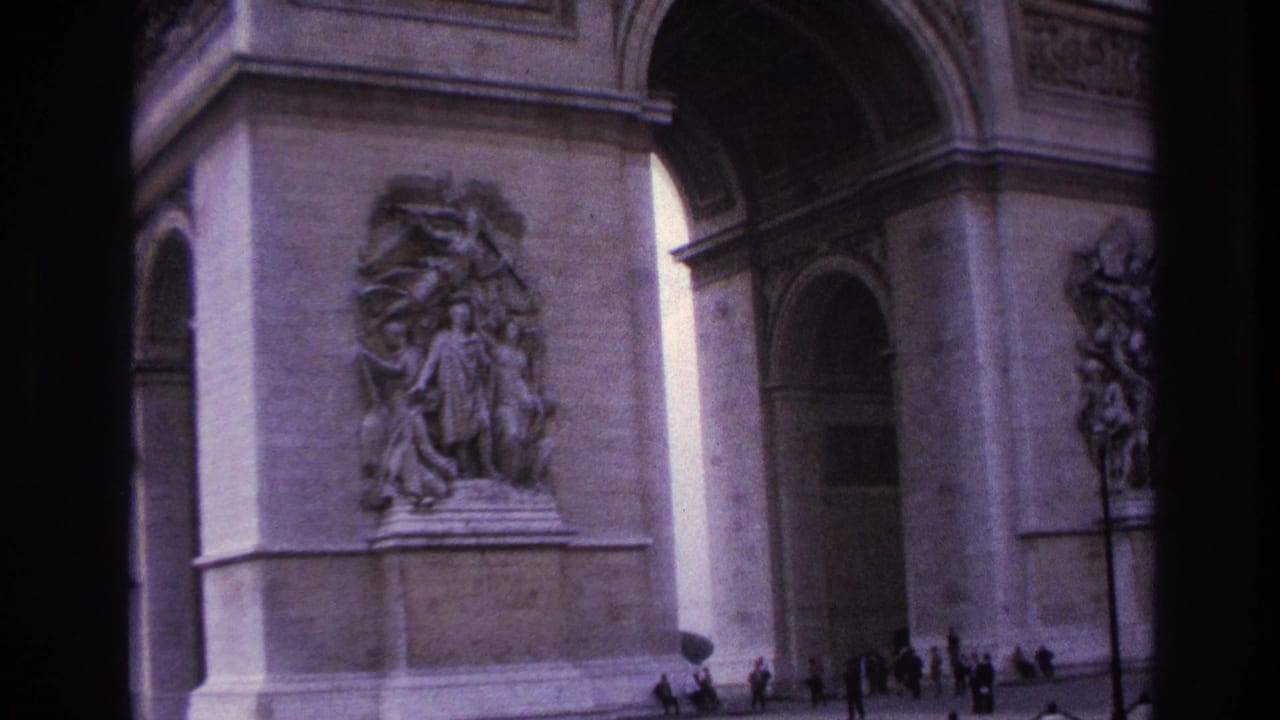 1967 Paris home-movie frame showing the Arc de Triomphe base, carved reliefs, arched openings, and small pedestrians near the monument.