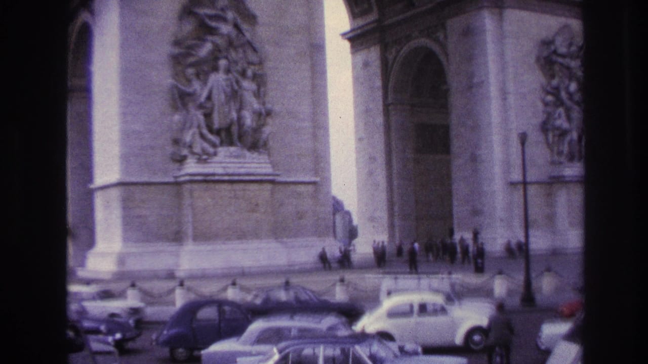 Arc de Triomphe with stone reliefs, pedestrians, streetlamp, and cars in the foreground.