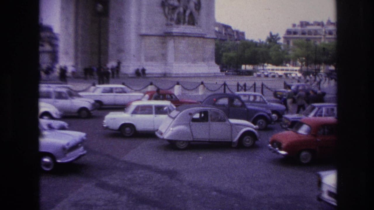 1967 Paris home-movie frame showing compact cars moving around the Arc de Triomphe traffic circle.