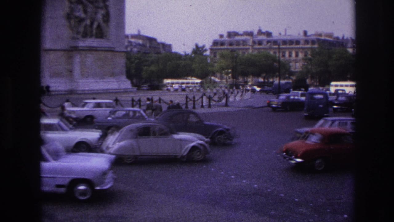Cars and vans move through a broad traffic circle beside a stone monument.