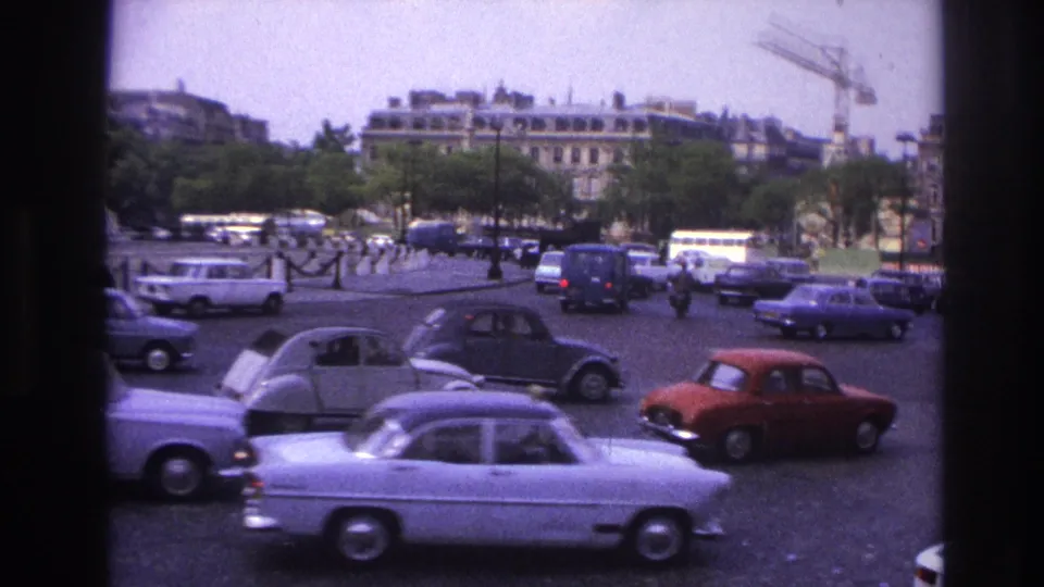 1967 Paris frame with cars, buses, pedestrians, trees, buildings, and a crane beyond the Arc de Triomphe area.