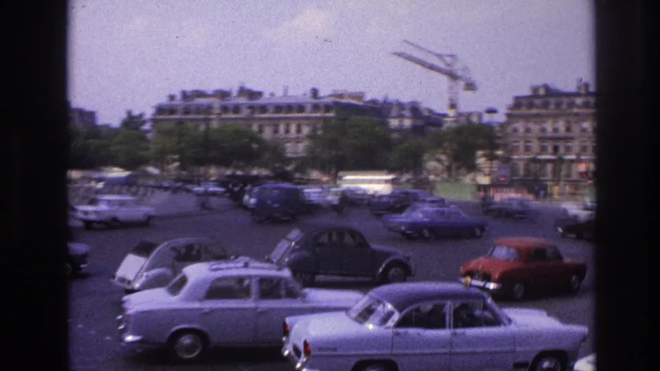 Final 1967 Paris home-movie frame showing dense roundabout traffic near the Arc de Triomphe with buildings beyond.