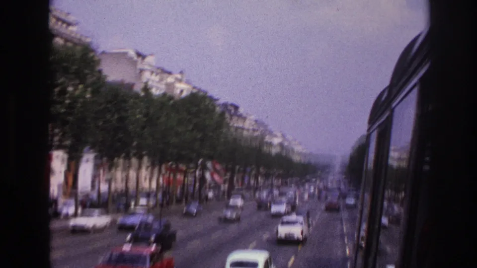 1967 Paris boulevard traffic viewed through a bus window, with rows of trees, apartment buildings, and cars moving along multiple lanes.