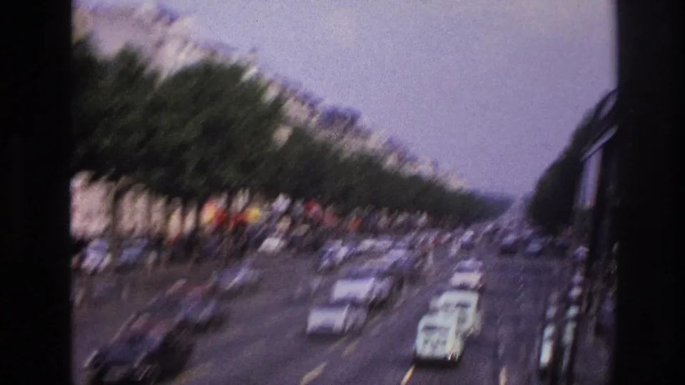 Motion-blurred 1967 Paris bus perspective with boulevard lanes, rows of trees, apartment blocks, and cars passing through the frame.