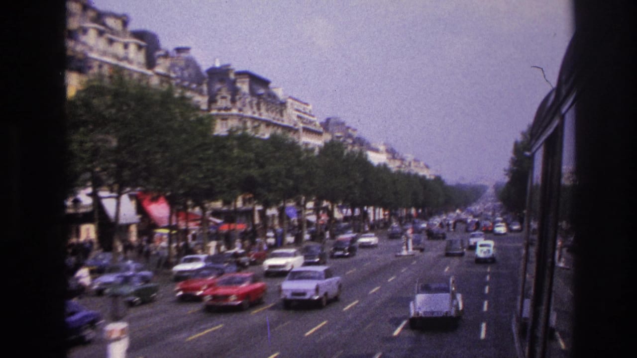 1967 Paris bus-window view over a broad boulevard with 1960s cars, rows of trees, and Haussmann-style buildings.