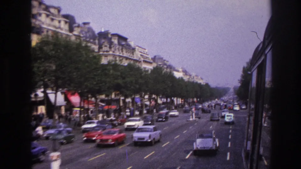1967 Paris bus-window view over a broad boulevard with 1960s cars, rows of trees, and Haussmann-style buildings.