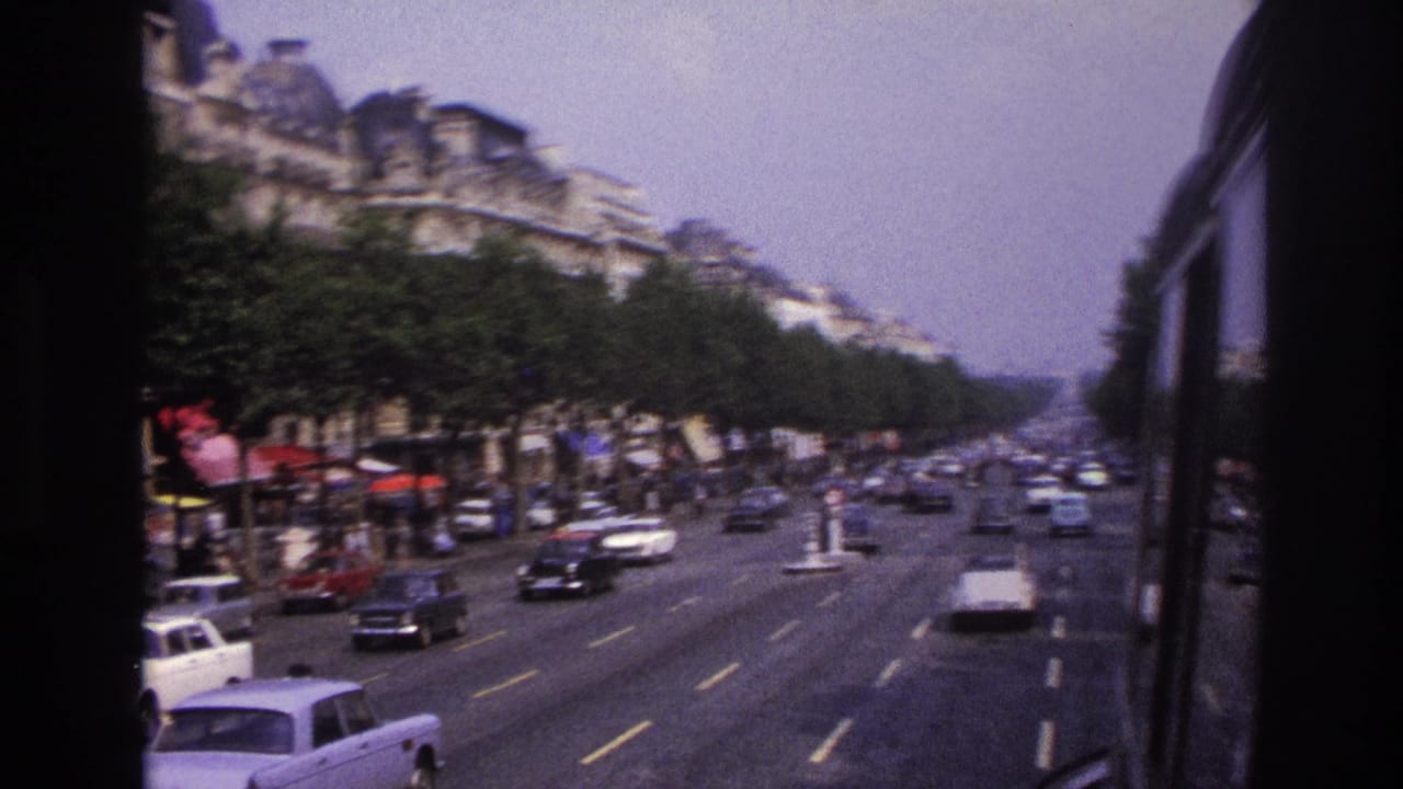 Traffic flows along a wide boulevard beside trees, storefronts, and tall residential buildings.