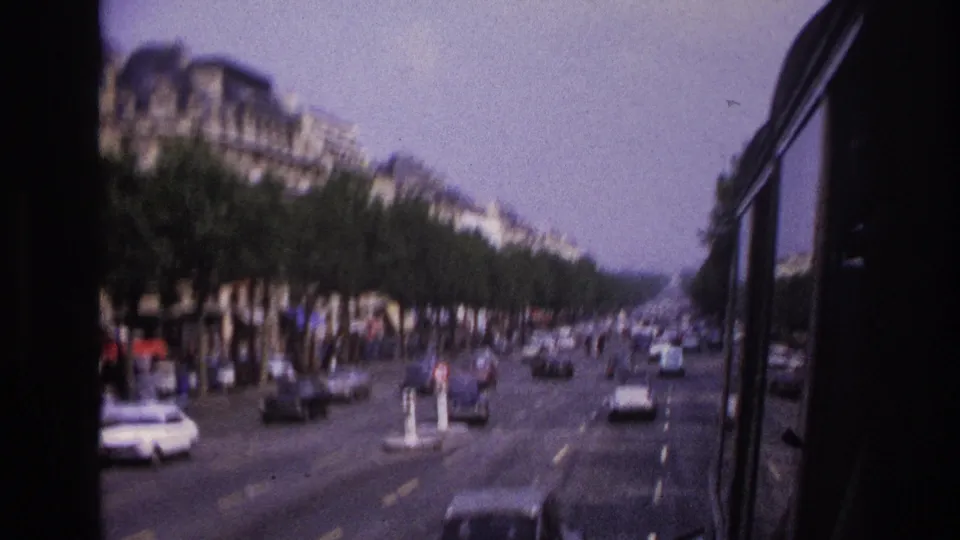 Motion-blurred 1967 Paris bus view, with cars on a wide roadway and tree-lined sidewalks below tall stone buildings.