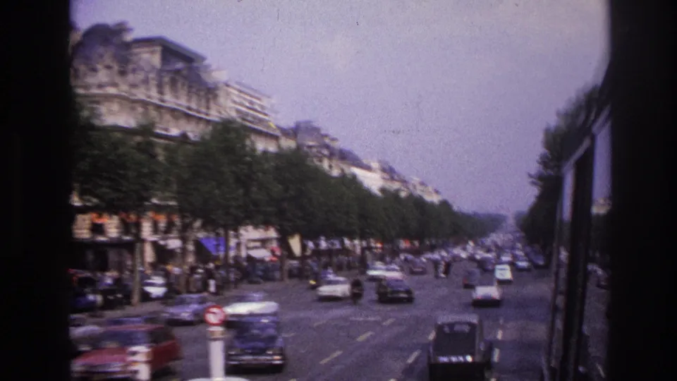 1967 Paris bus perspective showing a busy multi-lane boulevard, dark and light cars, sidewalk trees, and Haussmann-style facades.
