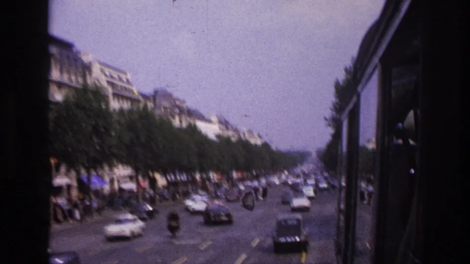 1967 Paris bus-window view looking along a tree-lined roadway with period cars, pedestrians, and soft home-movie blur.
