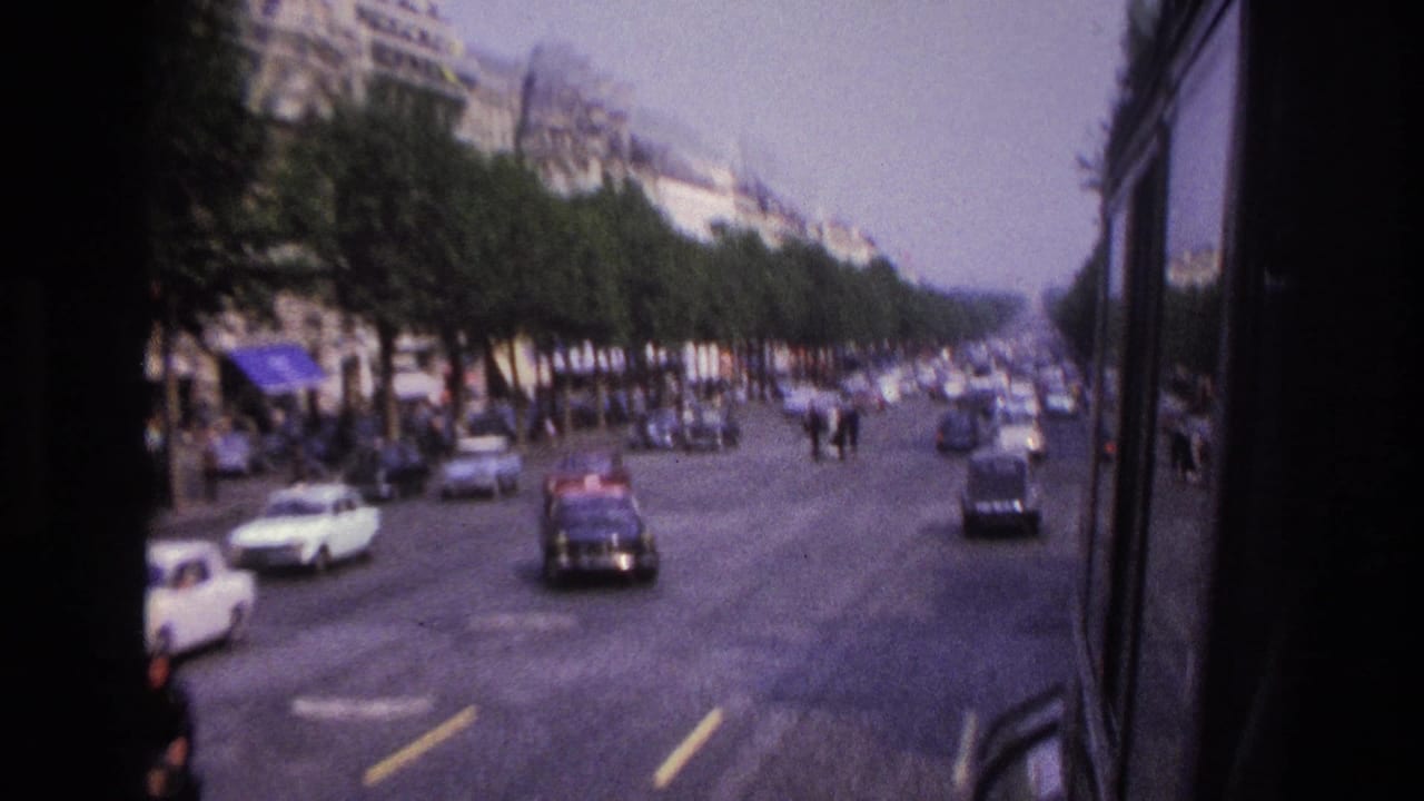 Moving bus view of roadway traffic with trees, cars, and distant pedestrians.